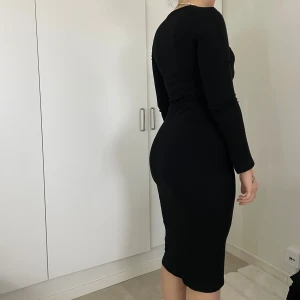 Svart långärmad klänning - Snygg svart klänning med lång ärm och v-ringning. Perfekt för en elegant look. Klänningen har en tight passform som framhäver figuren.