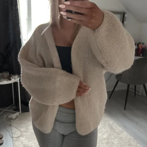 Beige stickad kofta - Mysig beige stickad kofta med en avslappnad passform. Perfekt för kyliga dagar och att mysa i hemma. Koftan har långa ärmar och en öppen design utan knappar.