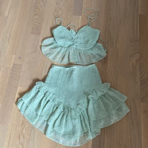 Grön blommig sett med volang - Söt grön sett med blommigt mönster och volangdetaljer. Toppen har smala axelband och snörning i ryggen för en justerbar passform. Perfekt för sommarens varma dagar. Den är även stretschig vilket gör att jag som storlek S också kan ha den 