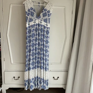 Vit och blå långklänning från L.O.G.G. - Härlig lång sommarklänning med blått och vitt mönster från L.O.G.G. Klänningen är ärmlös och v-ringad både från och bak med knytband i ryggen. Storlek 40. 