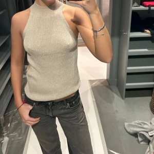 Beige ribbad linnetopp från Massimo Dutti - Snygg beige ribbad linnetopp från Massimo Dutti. Toppen är ärmlös med en hög hals och tillverkad av italienskt garn. Perfekt för en stilren look.
