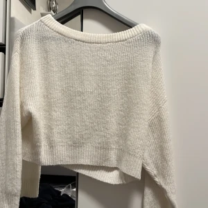 Vit stickad tröja - Säljer en vit stickad tröja med en croppad design. Tröjan har långa ärmar och en rund halsringning. Perfekt för kyligare dagar och kan enkelt matchas med olika outfits.