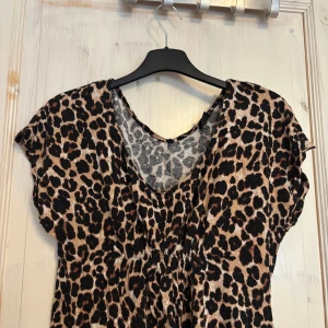 Leopardmönstrad topp från Gina Tricot - Snygg leopardmönstrad klänning från Gina Tricot i storlek XS men passar även S. har en v-ringad hals och korta ärmar. Perfekt för att fest/sommar. Insydd midja som gör vilket gör den figursydd i midjan.