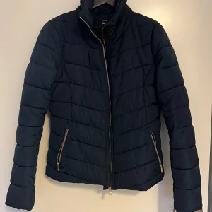 Marinblå dunjacka - Figursydd dunjacka från ONLY med gulddetaljer. Sitter verkligen som en smäck på, helt lagom längd och perfekt för kyliga dagar. Finns inga sminkfläckar i kragen