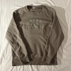 Beige sweatshirt från C.P. Company - Säljer en stilren beige sweatshirt från C.P. Company med broderad logga på bröstet. Tröjan är köpt direkt från butik och är i nyskick då den inte är använd mer än en handfull gånger. Har ni några funderingar är det som alltid bara att höra av sig!