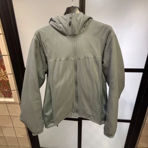 Grå/blå jacka från Arc'teryx - Säljer en stilren grå/blå jacka från Arc'teryx med huva och dragkedja. Perfekt för utomhusaktiviteter med sin funktionella design. Jackan har långa ärmar och är tillverkad i ett lätt syntetmaterial. Skicket är 7/10, lite små märken men inget man ser. Blir så på polyesterjackor. Size M men passar också S