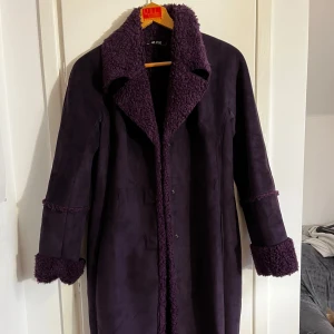 Lila kappa - Snygg mjuk kappa från AB Jeans med fluffigt foder och detaljer på krage och ärmslut. Perfekt för höst/vår. Går att knyta med ett band eller bara knäppa🪐