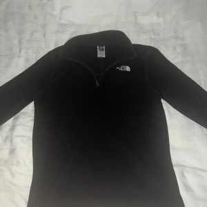 Svart fleece tröja från The North Face - Säljer en svart fleece tröja från The North Face med halv dragkedja och hög krage. Perfekt för kyliga dagar och outdoor-äventyr. Tröjan har långa ärmar och är supermjuk och bekväm. 