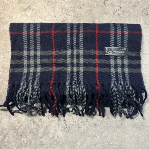Halsduk från Burberry - Snygg halsduk från Burberry i 100% lammull. Den har en klassisk design med fransar i ändarna och rutigt mönster. Perfekt för att hålla dig varm och stilren under kyliga dagar. 150Cm och är 10/10 skick. OBS den är svart‼️