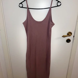 Rosa ribbad klänning - Säljer en stilren rosa/lila ribbad klänning med smala axelband. Perfekt för en avslappnad look. Klänningen har en enkel design och är lätt att matcha med olika accessoarer.