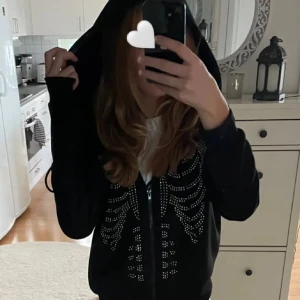 Svart hoodie med glittrig detalj - Säljer en svart hoodie med en cool glittrig design framtill. Den har en bekväm passform och en praktisk huva. Perfekt för en avslappnad stil.