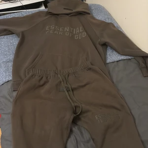 Fear of God Essentials off black tracksuit  - Säljer en Fear of God Essentials tracksuit i färgen off black. Storlek L men passar M. Bra kvalitet, men har ett pyttelitet hål i fickan. Priset går att diskutera och man kan köpa byxorna och hoodien enskilt. 