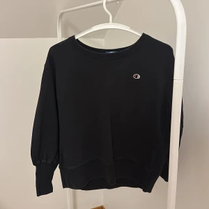 Svart sweatshirt från Champion - Säljer en klassisk svart sweatshirt från Champion med rund hals och det ikoniska Champion-logotypen på bröstet. Perfekt för en avslappnad stil. Tröjan har långa ärmar och ribbade muddar vid ärmslut och nederkant.
