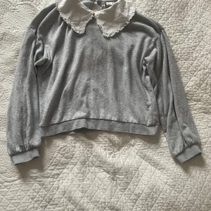 Grå tröja med vit krage från H&M Divided - Säljer en stilren grå tröja från H&M Divided med en vit spetskrage. Tröjan har långa ärmar och en bekväm passform. Perfekt för en avslappnad men ändå chic look. Kontakta mig för mer info eller köp direkt! 😊