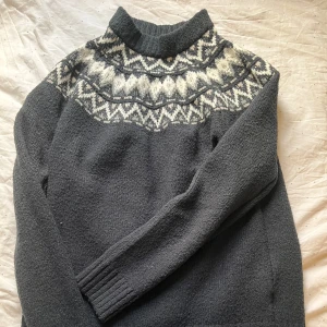 Mörkgrå stickad tröja med mönster - Säljer en mysig mörkgrå stickad tröja från 157 med ett klassiskt vitt mönster runt halsen. Tröjan har långa ärmar och en hög krage som håller dig varm under kyliga dagar. Perfekt för höst och vinter!