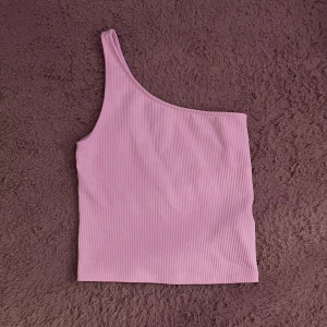 Rosa oneshoulder topp från Gina Tricot - Snygg rosa oneshoulder topp från Gina Tricot i ribbat material. Perfekt för en trendig look med sin unika design och mjuka känsla. Passar utmärkt till både jeans och kjol för en stilren outfit. 