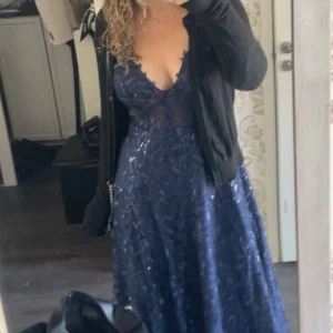 Mörkblå Balklänning  - En v ringad Balklänning i bra skick, den har en slits på sidan, vilket gör det luftigt och bekvämt. Blixtlås i ryggen.Ny pris 1843kr. Den är från JJs house.