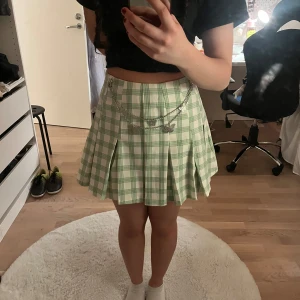 Grön och vit  kjol med kedjedetalj - Fin kjol i grönt och vitt rutmönster. Kjolen har en kedja med fjärilar💕