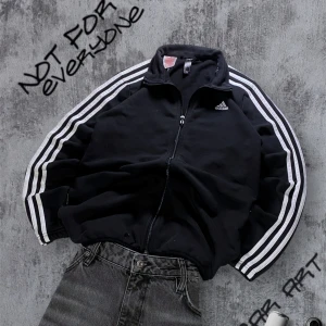 Retro Adidas Sweatshirt - Säljer en svart tröja från Adidas med de klassiska tre ränderna längs ärmarna. Jackan har dragkedja framtill och en liten Adidas-logga på bröstet samt 2 fickor. Perfekt för sportiga tillfällen eller en avslappnad stil. Skulle säga att den passar storlek S
