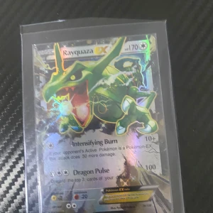 Rayquaza EX Pokémonkort - Säljer ett Rayquaza EX Pokémonkort med holografisk effekt. Kortet har attacker som Intensifying Burn och Dragon Pulse. Perfekt för samlare eller spelare som vill förstärka sin kortlek. Kortet är i en skyddande plastficka.