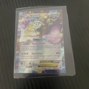 Aegislash EX Pokémonkort - Säljer ett Aegislash EX Pokémonkort med 170 HP. Kortet har förmågan Mighty Shield och attacken Slash Blast. Det är en del av serien från 2014 och har ett holografiskt utseende. Perfekt för samlare eller spelare som vill stärka sin kortlek!