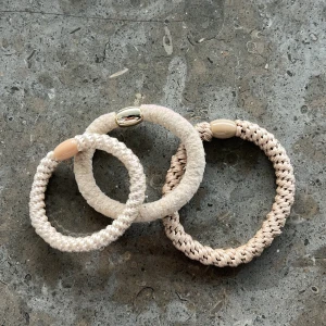 Tre beige kknekki armband - Säljer tre snygga beige kknekki armband. Två av dem har en dekorativ pärla i plast och ett har en metallisk detalj. Perfekta för att ge en bohemisk touch till din stil.