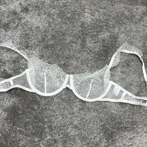 Vit spets-bh - Elegant vit bh i spets med blommigt mönster. Den har justerbara axelband och en klassisk bygel för extra stöd. Perfekt för att känna sig både bekväm och stilfull.