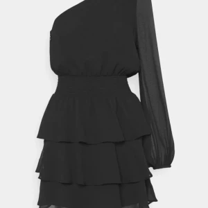 Svart oneshoulder klänning med volanger - Snygg svart oneshoulder klänning med volanger och lång ärm. Perfekt för en kväll ute eller en speciell tillställning. Den har en elastisk midja som ger en smickrande passform.