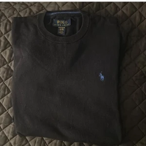 Svart tröja från Ralph Lauren - Säljer en klassisk svart tröja från Ralph Lauren med det ikoniska blå logotypbroderiet på bröstet. Tröjan har en rund halsringning och är perfekt för en stilren look. Passar bra till både jeans och chinos. (Kolla andra annonsen som är såld för mer information)