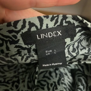 Mönstrad omlottkjol från Lindex - Säljer en snygg omlottkjol från Lindex med ett coolt mönster i svart och grön. Kjolen har en knytning i midjan och är perfekt för en avslappnad stil. Den är tillverkad i ett lätt och bekvämt material.