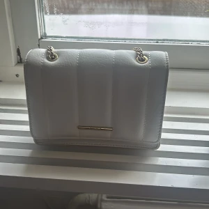 Vit quiltad axelväska med kedja - Snygg vit axelväska med quiltad design och guldfärgad kedja. Perfekt för att ge en stilren touch till din outfit. Väskan har en elegant och kompakt form, vilket gör den lätt att bära med sig.🩷