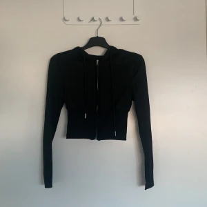 Svart croppad hoodie från Shein - Säljer en svart croppad hoodie från Shein. Den har en dragkedja framtill och långa ärmar. Perfekt för en casual look. Materialet är polyester vilket gör den mjuk och bekväm att bära.