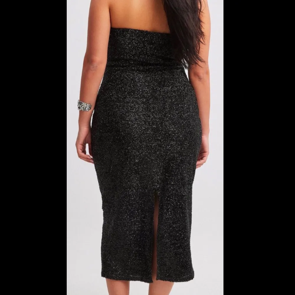 Snygg svart axelbandslös klänning med glittrigt material som ger en festlig look. Klänningen har en tight passform och en slits baktill för extra rörelsefrihet. Perfekt för en kväll ute eller en speciell tillställning. Klänningen är endast använd en gång🥰. Mekot.