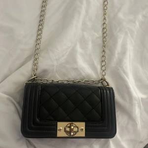 Svart quiltad axelväska med kedja från NELLY  - Snygg svart axelväska med en fin form och lätt att styla. Väskan e lite skavd på spännet och kedjan men inget ja själv tycker uppmärksammas så mycket när man har på sig den💗💗.