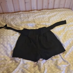Svarta shorts med knytband från H&M strl 36 - Snygga svarta shorts från H&M med ett knytband i midjan. Bekvämt tyg, lite som kostymbyxor. 