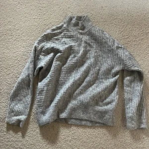 Grå ribbad polotröja - Säljer en stilren grå ribbad polotröja med långa ärmar. Perfekt för kyligare dagar med sin höga krage och mjukt material. Passar bra till både jeans och kjol för en avslappnad look.