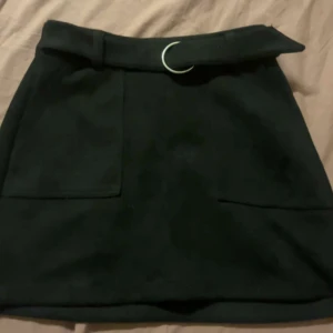 Svart kjol från Bershka - Snygg svart kjol från Bershka med ett stilrent bälte och fickor framtill. Kjolen har en dragkedja baktill för enkel på- och avtagning. Perfekt för en chic look!