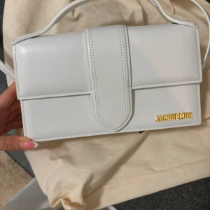 Vit axelväska från Jacquemus - Bambino Large - Snygg vit axelväska från Jacquemus i skinn. Väskan har en stilren design med ett guldfärgat logotypdetalj på framsidan. Perfekt för att ge en elegant touch till din outfit.
