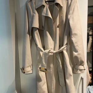 Trenchcoat  - Trenchcoat från Primark. Jättefin beige färg, och lagom lång!   Liten i storleken!!! Jag brukar ha 36 eller 38 och den passar mig! 