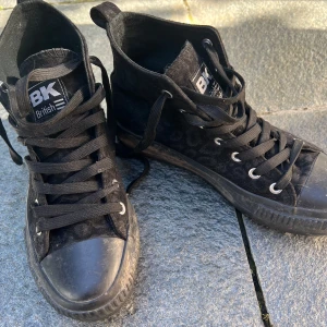 Svarta sneakers från British Knights - Säljer ett par svarta sneakers från British Knights i modellen Kaya Mid. Skorna har ett coolt leopardmönster och är i sammetslinande matetial. De har snörning framtill och en robust sula som ger bra grepp. Perfekta för både vardag och fest!