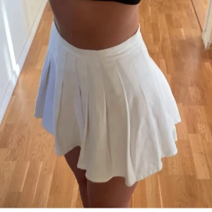 Vit kortkjol - Säljer en superfin vit kortkjol med veckad design. Perfekt för sommardagar eller en festlig kväll. Kjolen har en klassisk stil och är lätt att matcha med olika toppar. Den är i bra skick och redo för nya äventyr!