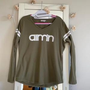 Olivgrön långärmad tröja från Aim'n - Säljer en snygg olivgrön långärmad tröja från Aim'n Casual. Den har en vit logga framtill och vita ränder på ärmarna. Perfekt för en avslappnad stil.. Tröjan är i bra skick och superbekväm att ha på sig!arm länd: 58cm . länd :68cm : bröst 48cm