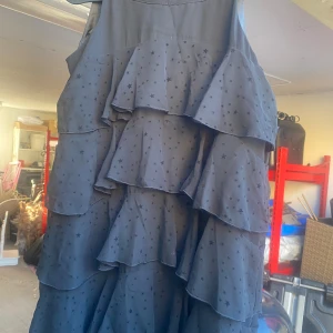 Svart volangklänning från H&M - Säljer en superfin svart klänning från H&M med volanger och ett stjärnmönster. Klänningen är ärmlös och perfekt för festliga tillfällen. Den har en lös passform och är gjord i ett lätt material som gör den bekväm att bära. Storlek 152.