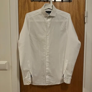 Vit finskjorta, XS - Säljer en av mina finskjortor som jag växt ur. Passformen är slim fit. Axelbredd: 40cm, längd: 71cm. Har bara använt den ett fåtal gånger så den är i fint skick. Se bilder. Frågor? Skicka ett dm!