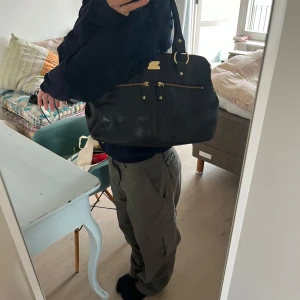 axelväska i skinn - Svart axelväska i skinn från MODALU. väskan är i mycket fint skick. Har flera fack/fickor. Dustbag medföljer. Om du önskar fler/närmare bilder är det bara att höra av dig✨ (måtten nedan är inte exakta utan kan skilja med några cm)