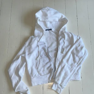 Vit hoodie från Brandy Melville - Säljer en supermjuk och bekväm vit hoodie från Brandy Melville. Den har en dragkedja framtill och en stor ficka på magen. Perfekt för en avslappnad stil eller mysiga dagar hemma. 🧡