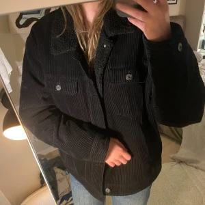 Jacka  - Vadderad jacka med teddy material i kragen och manchestertyg på utsidan. Den är varm och skön med en stor innerficka och fickor på sidan. 