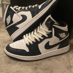 Nike Air Jordan 1 Mid i vit och marinblå - Säljer ett par Nike Air Jordan 1 Mid som är i 9/10 i skick använt fåtal gånger kvitto finns skriv till mig om ni vill ha mer bilder eller om ni undrar något😀