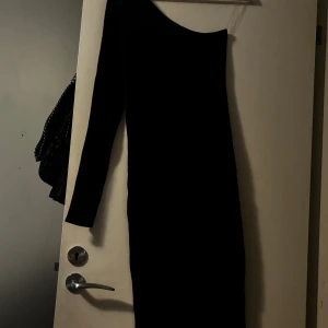 Svart oneshoulder klänning från Chiquelle - Säljer en elegant svart oneshoulder klänning från Chiquelle. Perfekt för festliga tillfällen med sin stilrena design och långa ärm. Klänningen är i storlek XS/S och sitter snyggt på kroppen.
