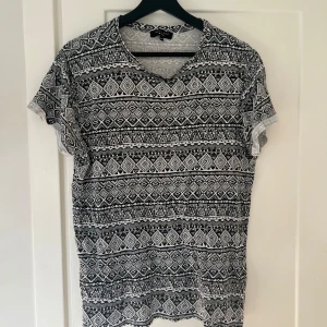 Mönstrad t-shirt från New Look Men - Säljer en snygg svartvit mönstrad t-shirt från New Look Men i storlek M. T-shirten har ett coolt geometriskt mönster och är perfekt för både vardag och fest. Den är kortärmad och gjord i ett bekvämt material. Passar perfekt till jeans eller shorts!